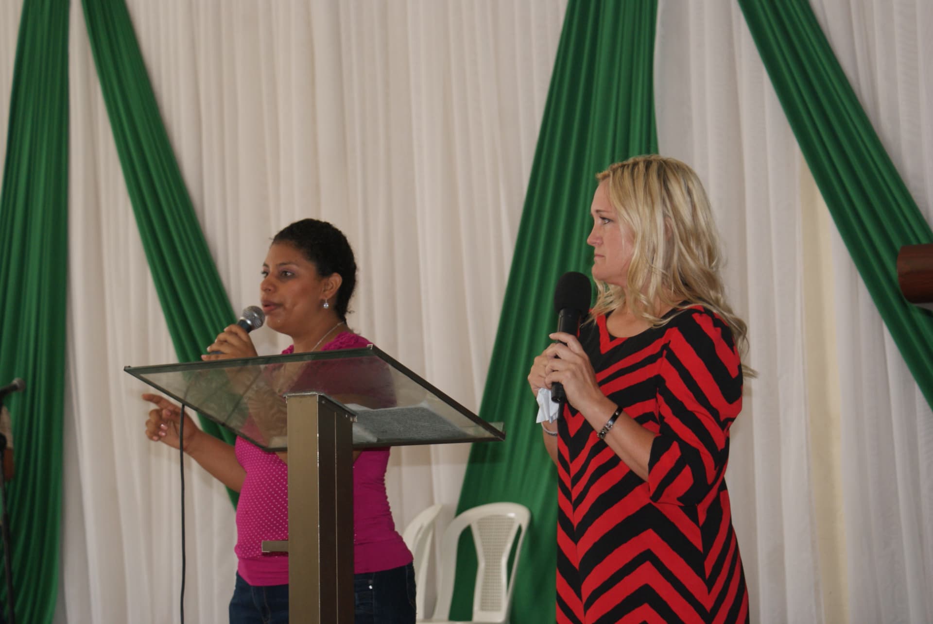 Shanna D. Olds in a red-and-black dress holding a microphone beside the woman translating her testimony